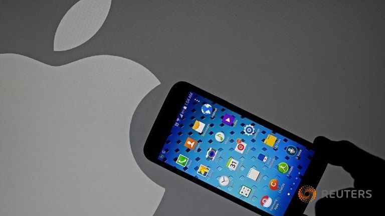 A Samsung Galaxy S5 smartphone is held next to a logo of Apple in this