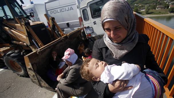 A migrant carrying a baby stands on a blocked road bridge over the Danube river between Serbia and Croatia