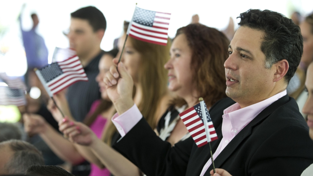 New citizens wave American flags during a U.S. Citizenship and Immigration Services naturalization ceremony in Miami in July