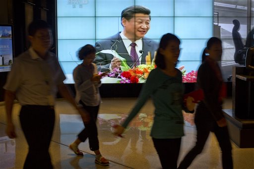 People walk past a large videoscreen showing Chinese President Xi Jinping during his trip to the United States from Chinese state broadcaster CCTV in an office building in Beijing Friday Sept. 25 2015. State media characterize Xis first state visit