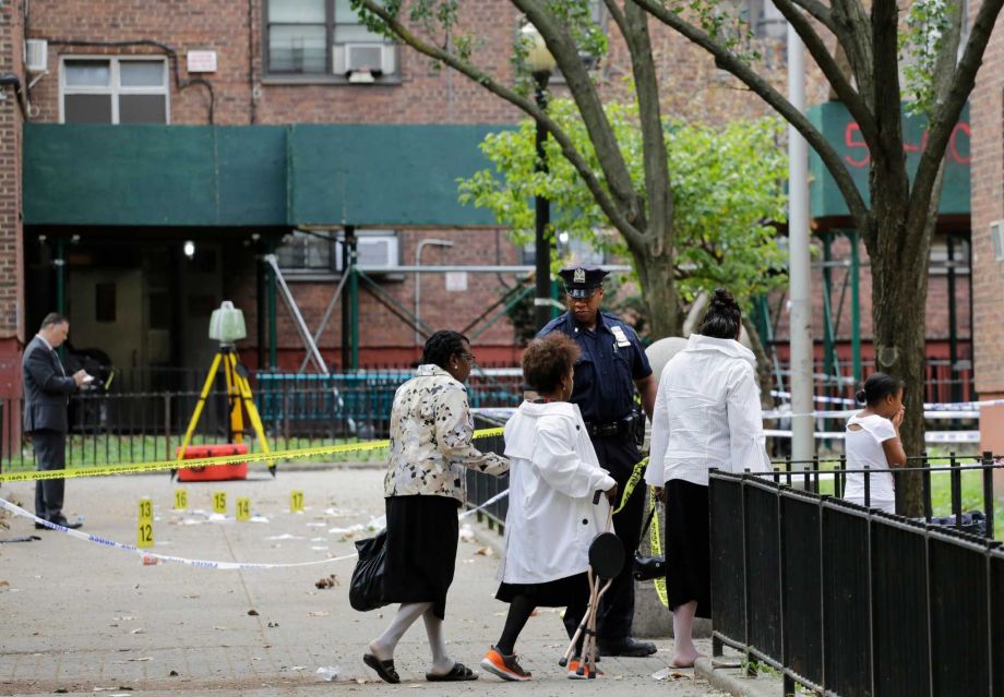 A girl right holds her hands to her mouth as she passes the scene of a triple homicide left Sunday Sept. 20 2015 at the Ingersoll Houses in the Brooklyn borough of New York. Three men were killed at the scene at 2 a.m. Sunday according to police. P