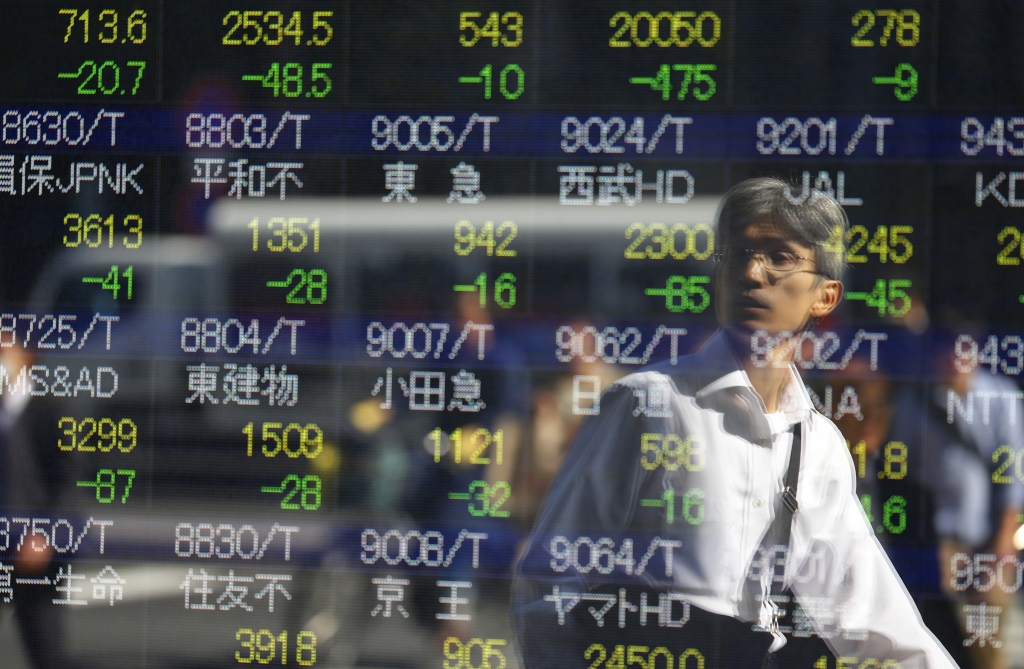 A man is reflected on an electronic stock indicator of a securities firm in Tokyo Wednesday Oct. 14 2015. Asian stock markets extended losses Wednesday following a drop on Wall Street as investors digested weak Chinese trade data and China's low inflat