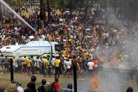 A demonstrator hangs on to a police water cannon during a protest over planned increases in tuition fees outside the Union building in Pretoria South Africa