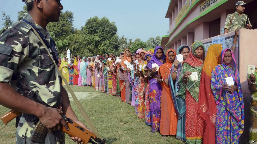 Indian security personnel guard as women voters stand in a queue to cast their votes at a polling station during the first of the five phase voting for state legislative assembly at Mahmoodpur village in Samastipur district of India’s eastern state Bih