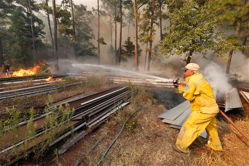 Firefighters work with heavy machinery to contain the fire near Smithville Texas Wednesday Oct. 14 2015. The Texas A&M Forest Service says challenging topography and uncontrolled fire lines has slashed the containment of the Bastrop County fire to 10