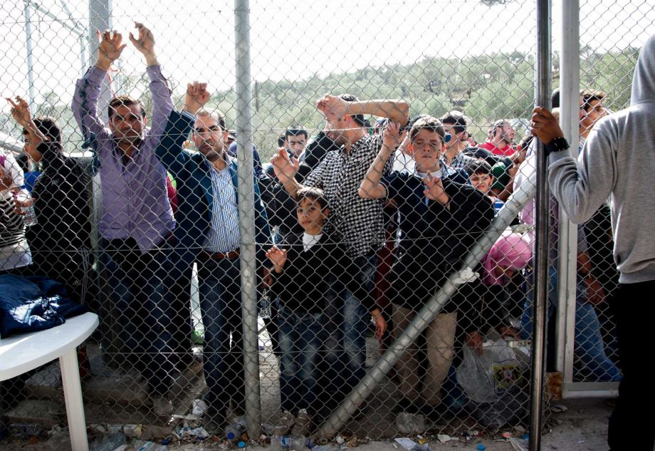 Migrants and refugees wait outside a fence of the Moria camp on the eastern Aegean island of Lesbos Greece Saturday Oct. 10 2015. Greece’s first “hotspot,” or migrant processing center will open over the next 10 days allowing migrants to be