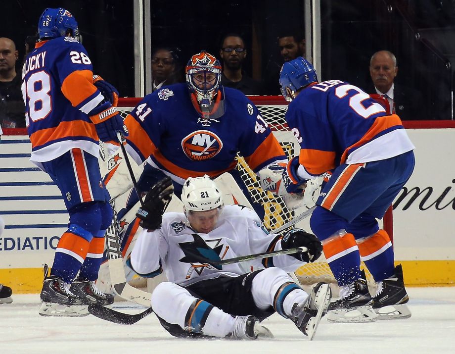 San Jose’s Ben Smith crumples to the ice in front of Islanders goalie Jaroslav Halak after being hit in the head with a puck