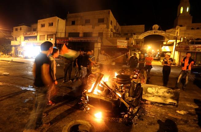 Palestinian youth stand next to a burning car belonging to an Israeli settler that was set on fire by Palestinians as it entered the northern Palestinian West Bank city of Nablus early