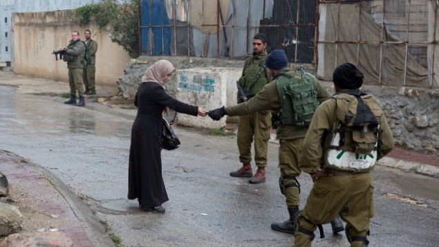 Israeli soldiers check the ID of a Palestinian woman near a Jewish enclave in Hebron