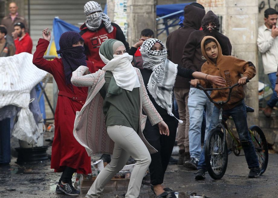 Palestinian young women throw stones toward Israeli security forces during clashes in the West Bank town of Hebron