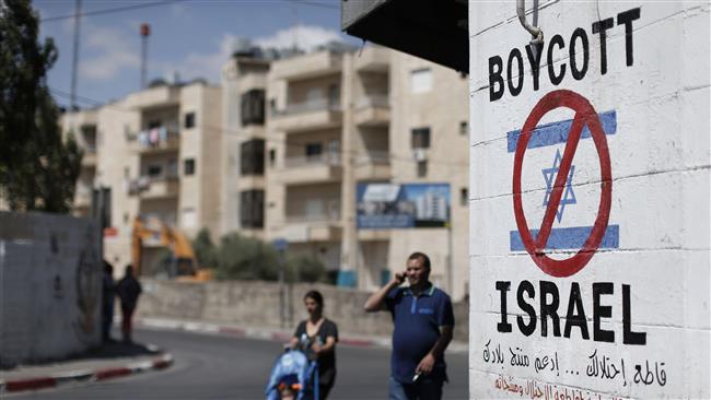 Palestinians walk past a sign painted on a wall calling to boycott Israeli products coming from settlements in the West Bank town of Bethlehem