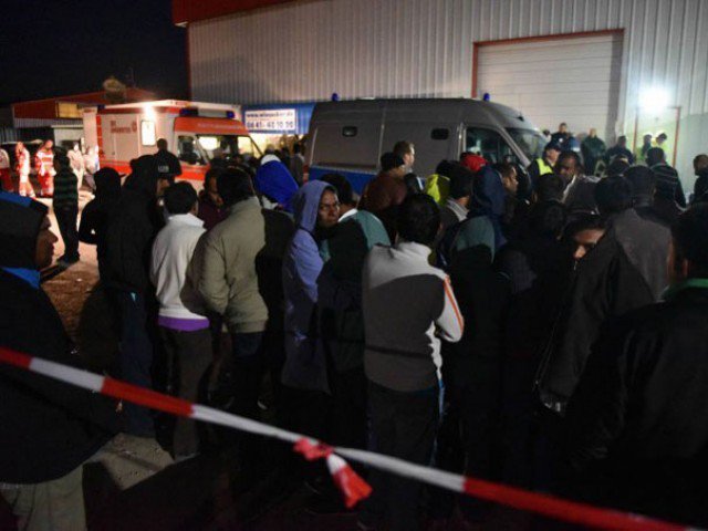 Refugees stand by rescuers and police officers outside a migrants shelter in Calden near Kassel