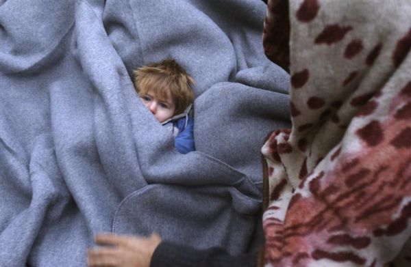 A migrant child is muffled up in blankets