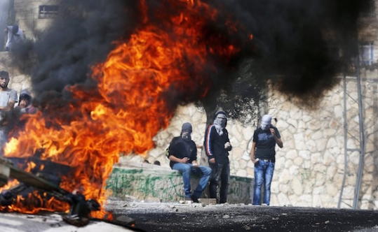 Stone-throwing Palestinian youths stand next to a fire during clashes with Israeli police in Sur Baher east Jerusalem on Oct. 7