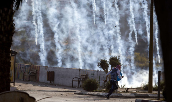 A Palestinian protester runs from tear gas fired by Israeli soldiers during clashes near Ramallah. Israelis on Saturday shot dead three Palestinians