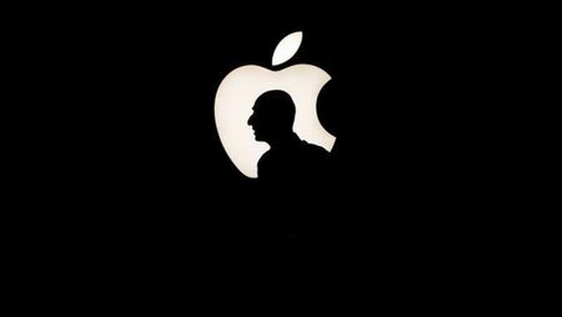 A man walks past a backlit Apple logo during an Apple media event in San Francisco California