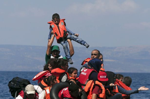 A refugee raises a child into the air as Syrian and Afghan refugees are seen on and around a dinghy that deflated some 100m away before reaching the Greek island of Lesbos