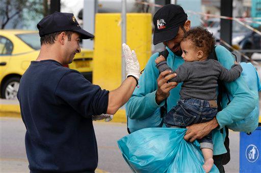 A coast guard officer plays with a child as his father holds him after their arrival from the Greek island of Lesbos at the Athens port of Piraeus Monday Oct. 19 2015. More than 600,000 people mostly Syrians have reached Europe since the beginning