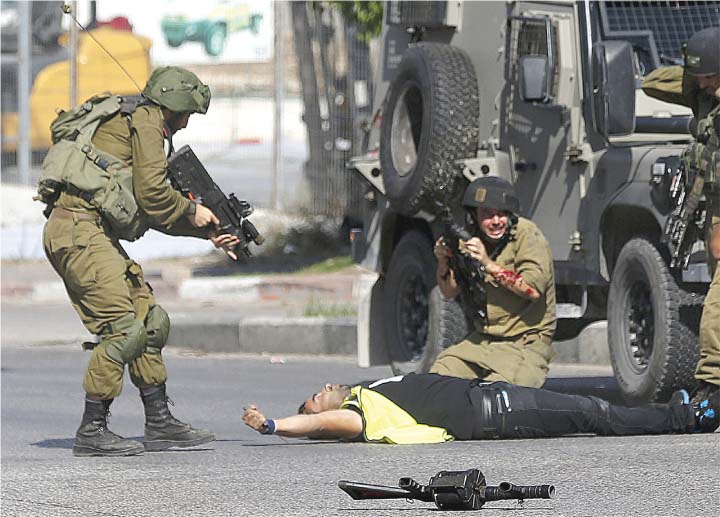 PGRAPHER – Israeli soldiers including one who was stabbed on the forearm, stand over the body of an alleged Palestinian attacker who was able to advance through a security cordon by pretending to be a local news