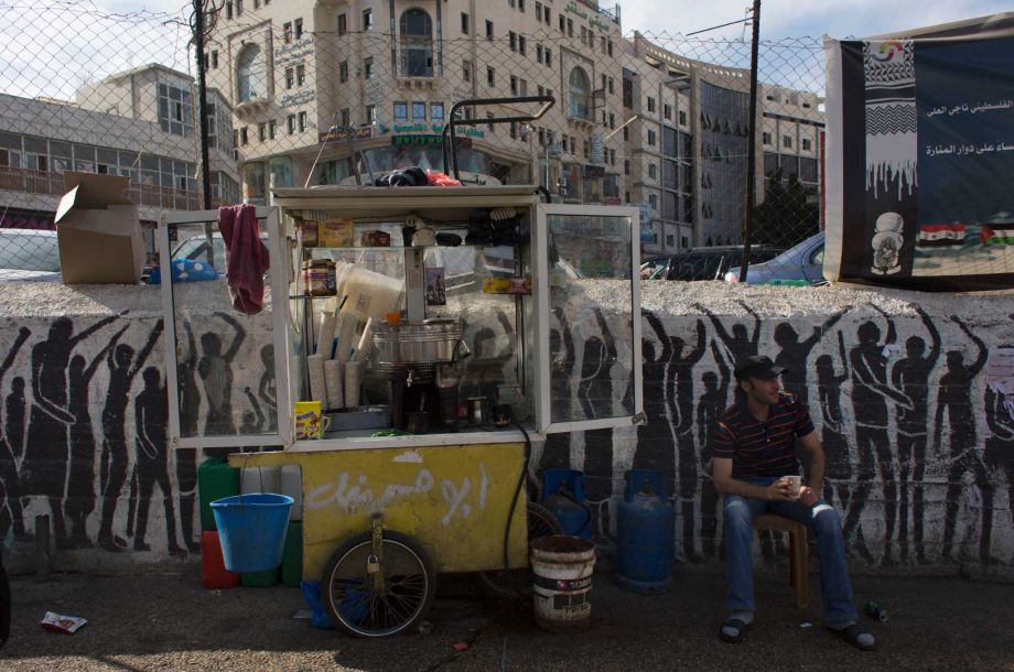 A Palestinian drink vendor drinks coffee and smokes a cigarette while he waits for customers in the West Bank city of Ramallah Tuesday Sept. 29 2015. The World Bank said the Palestinian economy has worsened for a third consecutive year. In a report rel