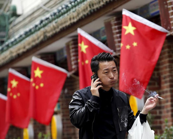 A smoker walks past Chinese national flags in front of a restaurant in Beijing