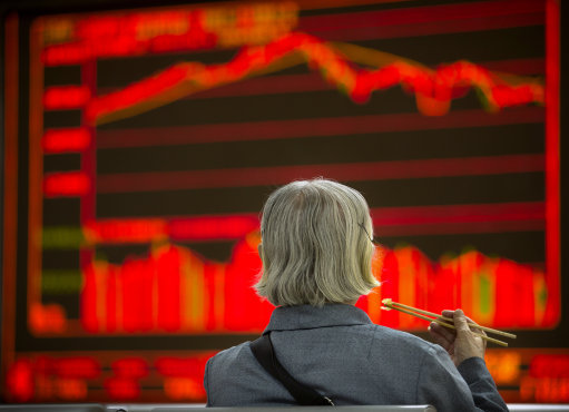 A Chinese investor eats lunch as she monitors stock prices at a brokerage house in Beijing- Mark Schiefelbein  AP