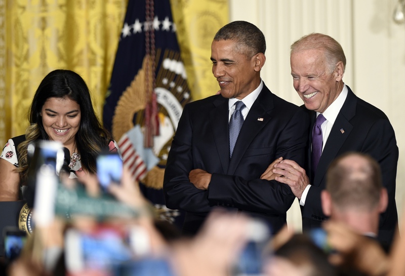 President Barack Obama center standing with Vice President Joe Biden right listens as Diana Calderon a student who has benefited from the Deferred Action for Childhood Arrivals program speaks at a reception in the East Room of the White House