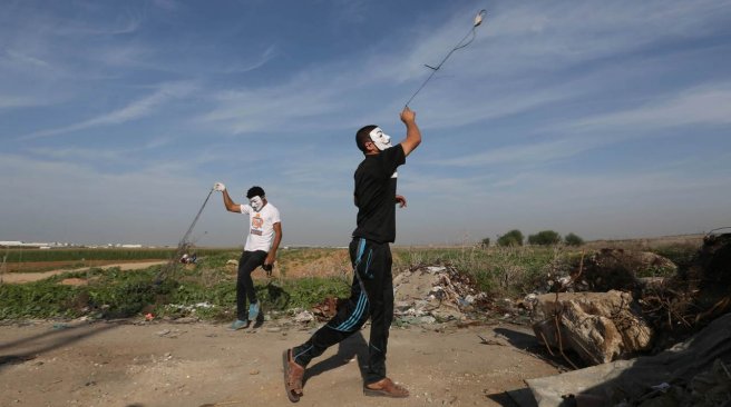 Palestinian protesters use slingshots to throw stones at Israeli security forces during clashes along the border with Israel on the eastern outskirts of Gaza City