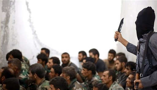 A fighter from the Islamic State armed with a knife and an automatic weapon is shown next to captured Syrian army soldiers and officers following the battle for the Tabqa air base in Raqqa Syria. (AP