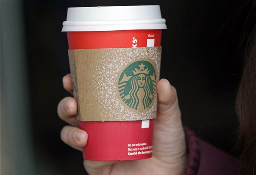 A customer carries a coffee drink in a red paper cup with a cardboard cover attached outside a Starbucks coffee shop in the Pike Place Market Tuesday Nov. 10 2015 in Seattle. It's as red as Santa's suit a poinsettia blossom or a loud Chri