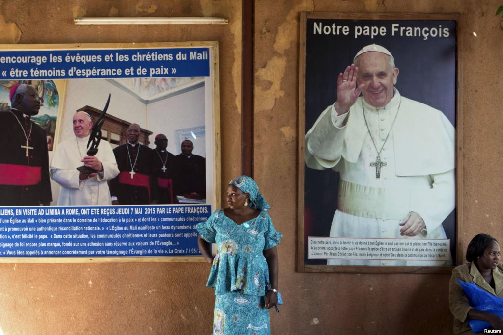 FILE- A woman stands in front of posters of Pope Francis on Nov. 8 2015 at the Martyrs of Uganda church in Bamako Mali