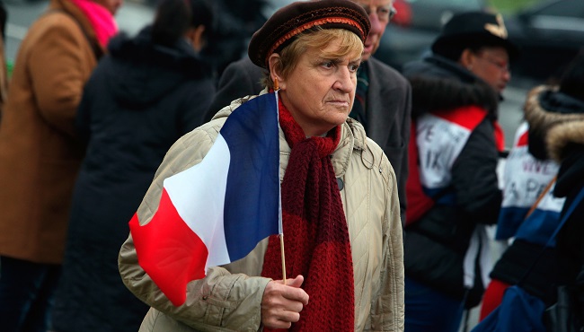 A woman holds a French flag outside the Invalides during a ceremony honoring those killed in the Nov. 13 attacks in Paris Friday Nov. 27 2015. France is mourning and honoring those killed in the attacks in a somber ceremony presided by French Preside