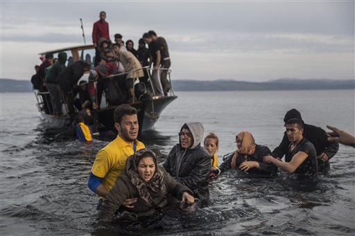 Greek lifeguards help refugees and migrants to disembark from a small boat after their arrival from the Turkish coast on the northeastern Greek island of Lesbos Monday Nov. 16 2015. Greek authorities say 1,244 refugees and economic migrants have been