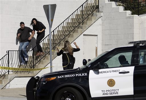 San Diego police officers assist a couple as they evacuate a building in San Diego on Wednesday Nov. 4 1015. A man with a high-powered gun was firing sporadically inside a San Diego apartment complex causing the city's nearby airport to stop plane