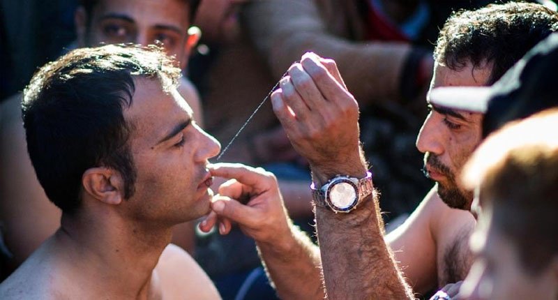 A man sews shut the mouth of a fellow migrant from Iran in protest at being held up at the Greece Macedonia border near Gevgelija