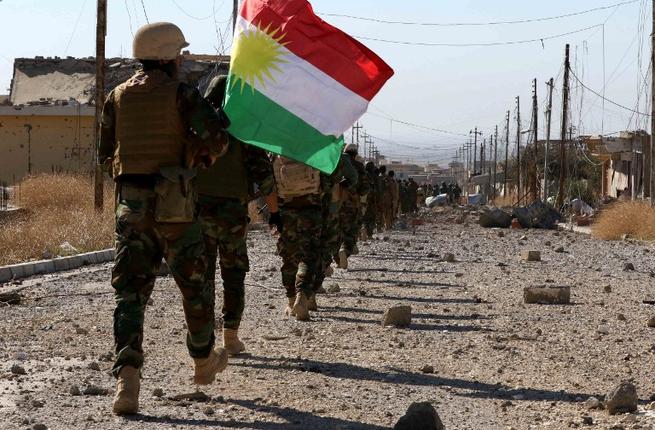 Peshmerga forces and Yazidi fighters hold a Kurdish flag while entering the northern Iraqi town of Sinjar in the Nineveh Province