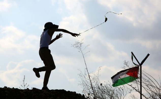 A protester hurls a stone next to a Palestinian flag during clashes with Israeli security forces in the West Bank town of Tulkarem