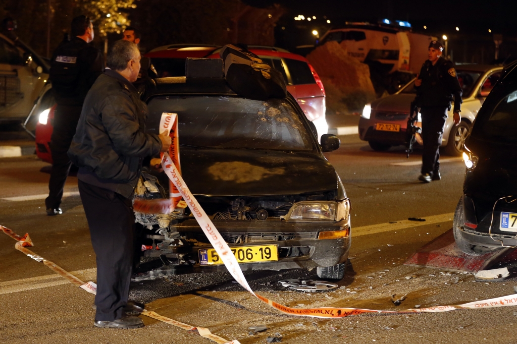 An Israeli forensic expert stands next to a car at the site of an attack that left one Israeli dead and eight wounded in the Jewish settlement bloc of Gush Etzion south of Jerusalem