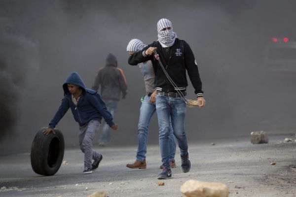 Palestinian protesters prepare to throw stones towards Israeli