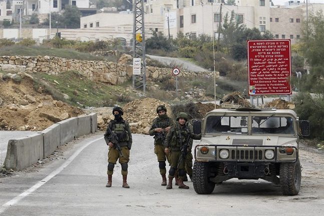 Israeli soldiers stand guard after the military blocked the road with an earth berm at one of the exits of the West Bank city of Hebron Saturday Nov. 7 2015. Three incidents took place Friday in Hebron the West Bank's largest city which has been the