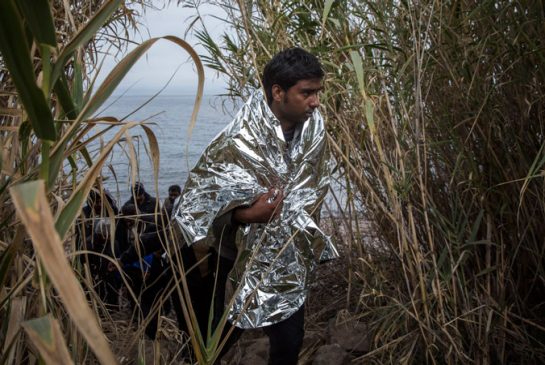 A Pakistani migrant wears a thermal blanket provided by volunteers as he leaves a beach after crossing the Aegean sea in a dinghy with other refugees and migrants from Turkey to the northeastern Greek island of Lesbos on Tuesday Nov. 24 2015