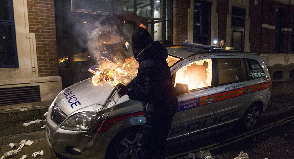 Anti-capitalist protesters attack a British police car during the Million Masks March organised by the group Anonymous near the Houses of Parliament in London