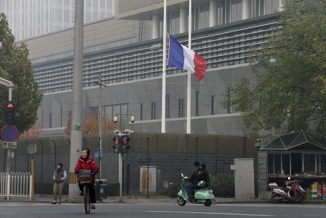 A cyclist and a motorist drive past a French national flag fluttering at half-mast to mourn for the victims killed in the Friday's attacks in Paris France