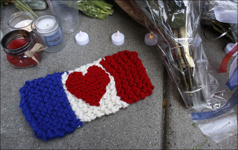 A knitted French flag with a heart design in the center rests on Sunday on the sidewalk next to candles outside the French Consulate in Boston