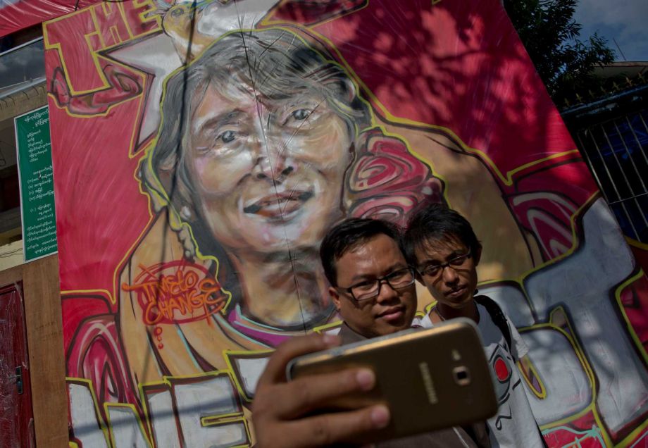 People mark a historic day Friday in the foreground of a portrait featuring Myanmar's opposition leader Aung San Suu Kyi after the landslide election in Yangon