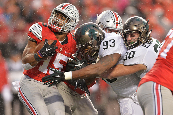 COLUMBUS OH- NOVEMBER 21 Ezekiel Elliott #15 of the Ohio State Buckeyes runs into Damon Knox #93 of the Michigan State Spartans and Riley Bullough #30 of the Michigan State Spartans at the line of scrimmage in the second quarter at Ohio Stadium on Nov