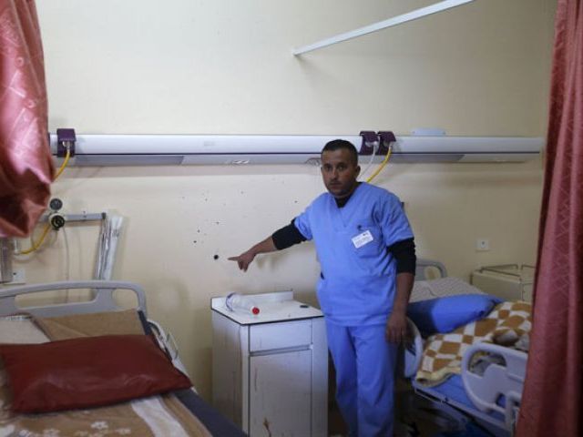 A medic shows to journalists a bullet hole in a wall surrounded by blood stains of a Palestinian man who was killed by Israeli undercover forces during a raid at Al Ahly hospital in the West Bank city of Hebr