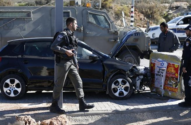 An Israeli border guard stands in front of a damaged car at the spot where a Palestinian man was shot by Israeli forces after reportedly ramming a vehicle into a number of Israeli troops wounding two soldiers and one border policeman at the Tapuah junct