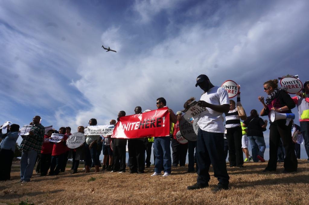 Food service workers protest outside American Airlines headquarters near D  FW Airport as an AA jet flies by. The protestors want customers like American Airlines and other carriers to pay food service companies more so those companies will improve and ben