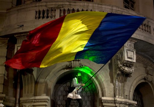 A man's face is illuminated by a laser torch as he waves a large Romanian flag after climbing the University building during the third day of protests joined by tens of thousands across the country calling for early elections in Bucharest Roman